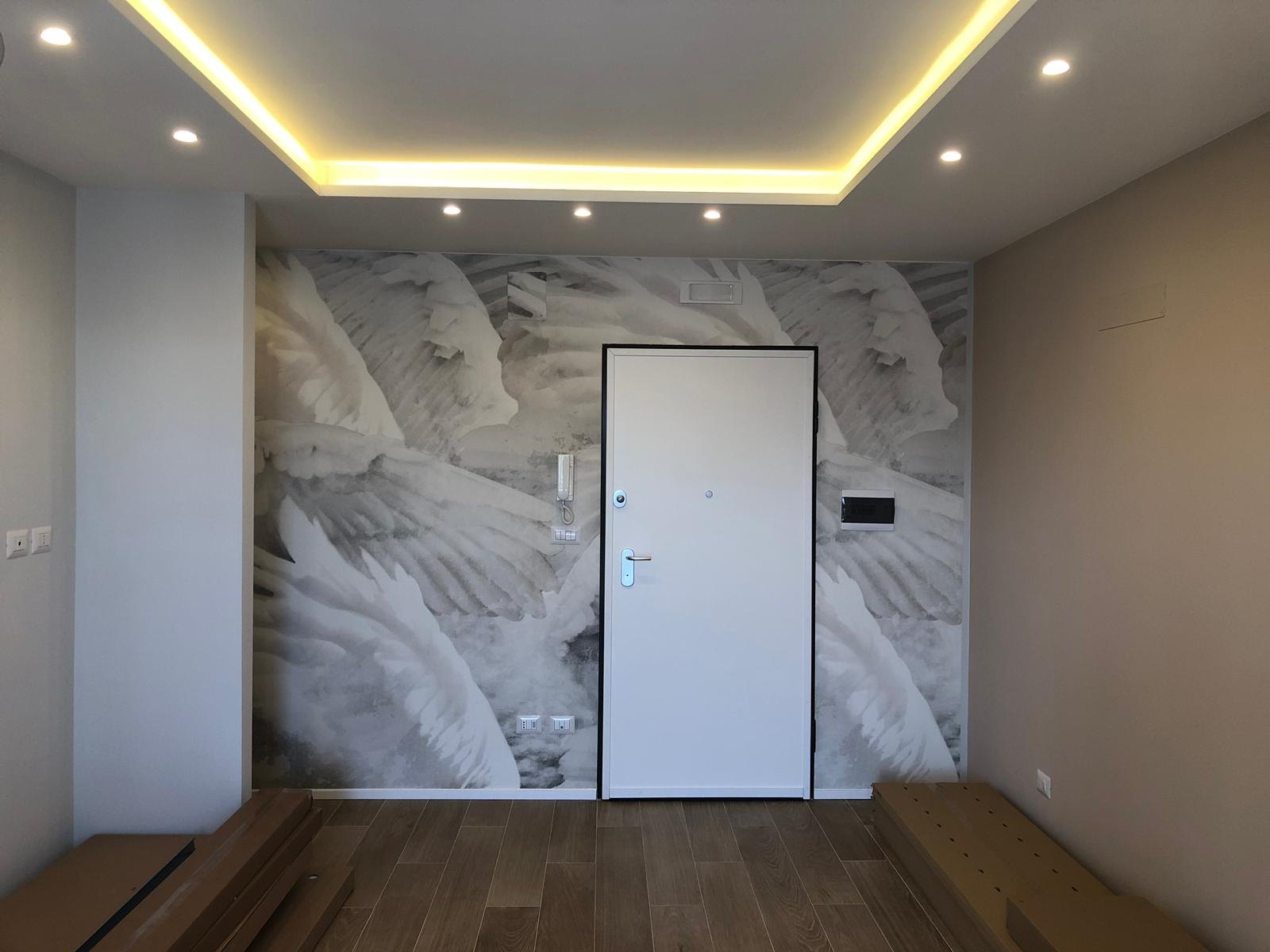 Ingresso con porta bianca, carta da parati a piume grigie, controsoffitto con LED caldi e pavimento effetto legno